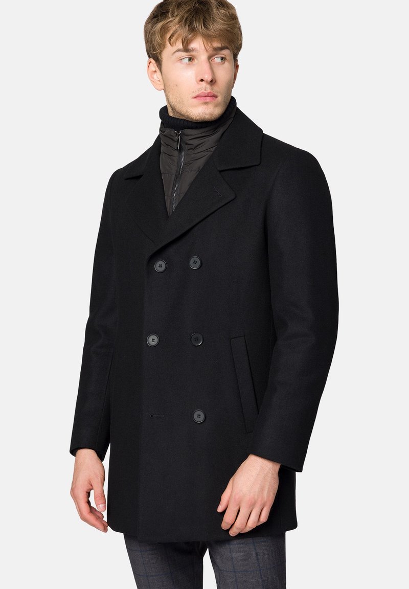 Czarny wełniany płaszcz dwurzędowy z dużymi guzikami, klapami oraz bocznymi kieszeniami; noszony na czarnej wewnętrznej warstwie zapinanej na zamek.