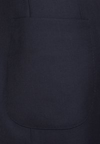 Granatowy materiał o teksturowanej powierzchni; posiada kieszeń łataną z zaokrąglonymi krawędziami i widocznymi detalami przeszycia.