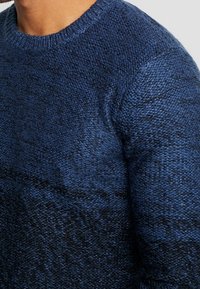Pull en tricot présentant un dégradé de nuances de bleu profond, encolure ronde, tissu texturé et poignets côtelés. Matière douce et chaude.