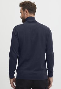 Mørkeblå genser med høy krage, ribbede ermer og nederkant. Stoffet ser glatt og mykt ut med en tettsittende design.