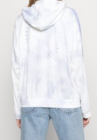 Bílá síťovaná bunda s kapucí a lehkým materiálem, která je zdobena jemným vzorem tie-dye a elastickými manžetami na lemu.