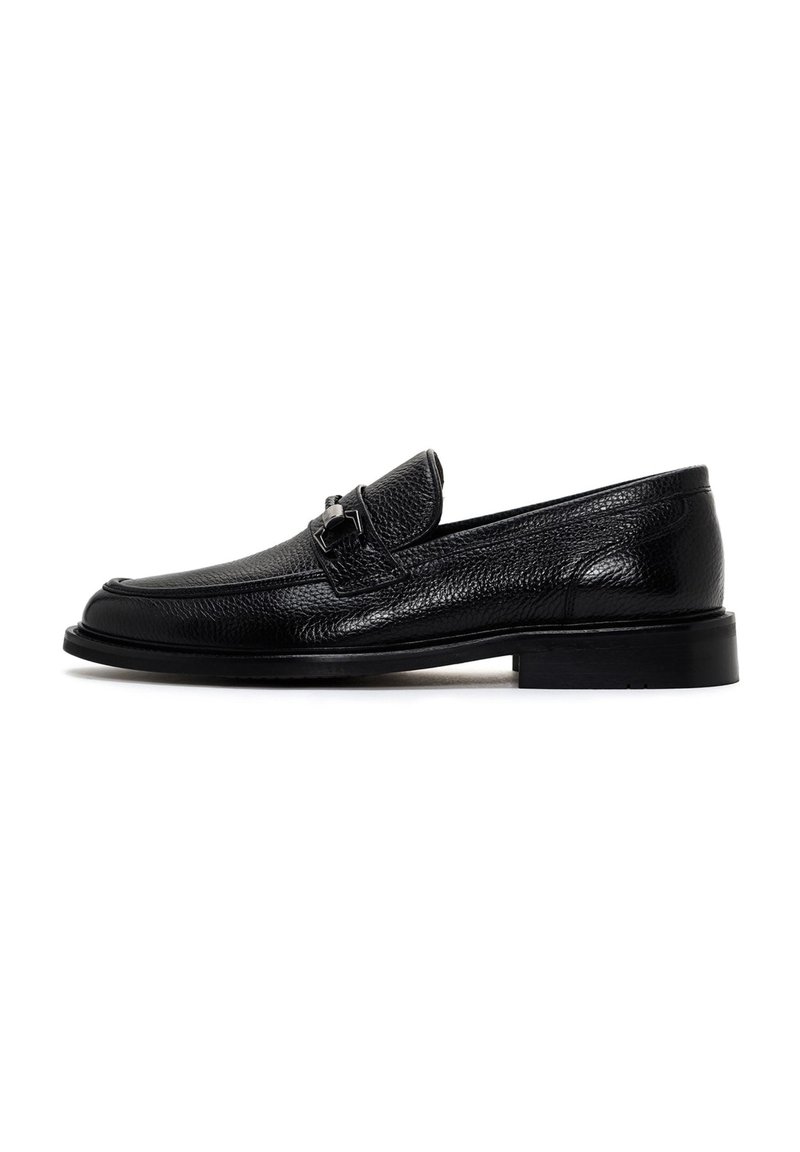 Mocasines de cuero negro con un acabado texturizado, diseño sofisticado, suela plana y detalle en metal plateado en la parte delantera.