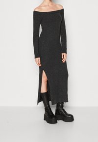 Schulterfreies, langärmliges, dunkelgraues Strickkleid mit einem Seiten-Schlitz, kombiniert mit schwarzen Schnürplattformstiefeln. Glatte Textur.