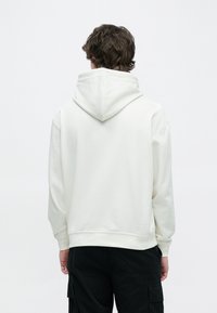 Άσπρο φούτερ με κουκούλα και κορδόνι, τσέπη καγκουρό και ριμπ μανσέτες. Μαλακό ύφασμα με λεία υφή. Η πίσω όψη δείχνει λεπτομέρειες ραφών.