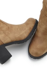 Brown suede ankle boots with a chunky black heel and rubber sole, featuring a smooth texture and stitched accents on the sides.