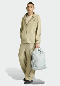 Beige lightweight jacket with hood and matching pants, featuring subtle geometric patterns; carrying a light grey backpack with a zip pocket.