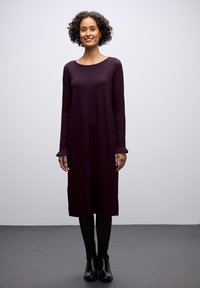 Abito lungo a maniche, di colore viola, con scollatura arrotondata e polsini a costine, realizzato in tessuto morbido, abbinato a stivali neri alla caviglia.