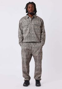 Ensemble en tissu texturé gris comprenant une veste à col avec deux poches poitrine et un pantalon élastique assorti, associé à des chaussures noires.