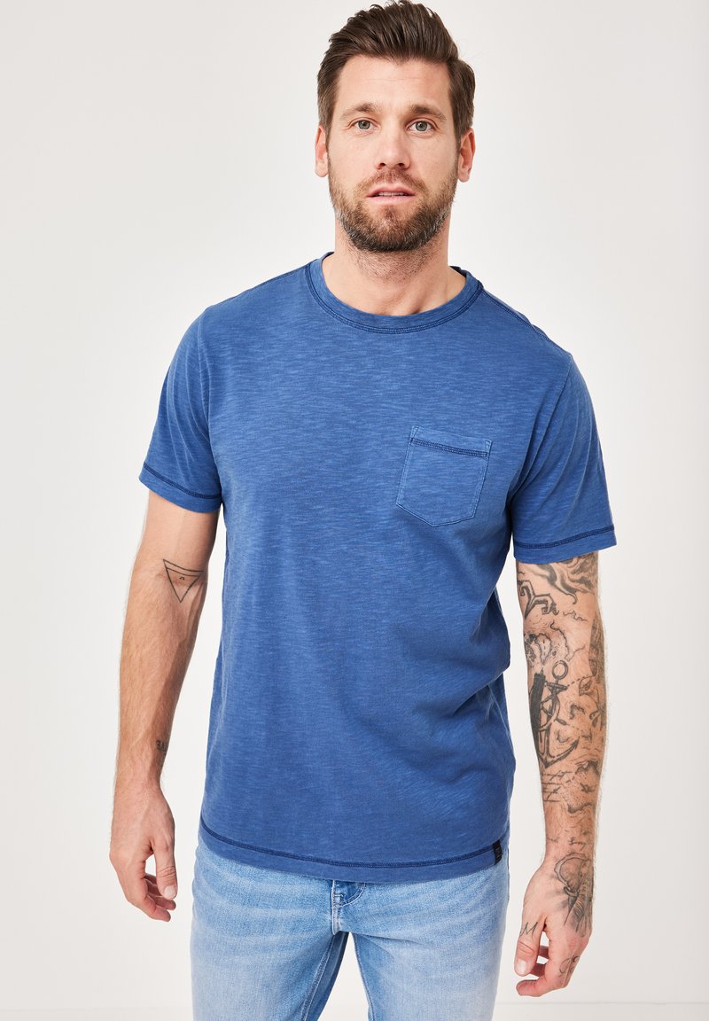 Blue short-sleeve t-shirt featuring a round neckline and a chest pocket. Soft texture with a subtle heather pattern. Worn with light jeans.