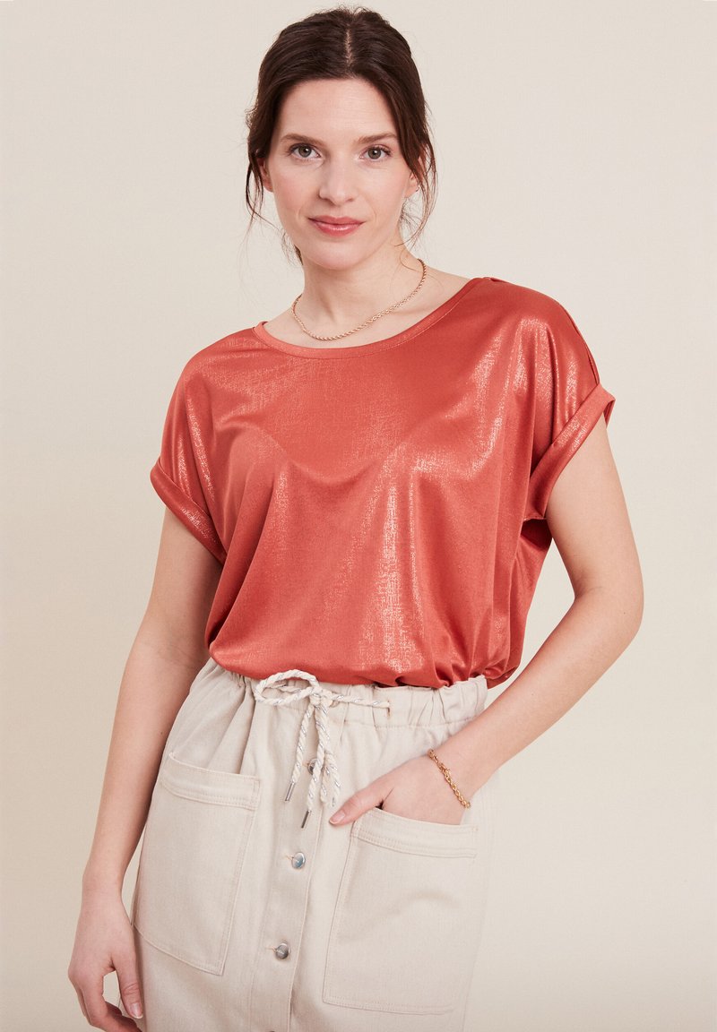 Glanzend, roestkleurig kort mouwen top met opgerolde manchetten, gecombineerd met een lichtbeige rok met een trekkoordtaille en knoopsluiting.