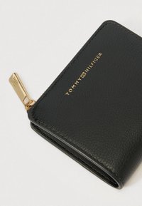 Μαύρο δερμάτινο πορτοφόλι με υφή, με χρυσό φερμουάρ και εγχάρακτο λογότυπο, συμπαγές ορθογώνιο σχέδιο.