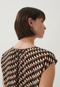 T-shirt met korte mouwen in een bruine basis met een golvend zwart-wit patroon. Heeft een geplooide achterkant en een ronde halslijn. Fijne stoftextuur.