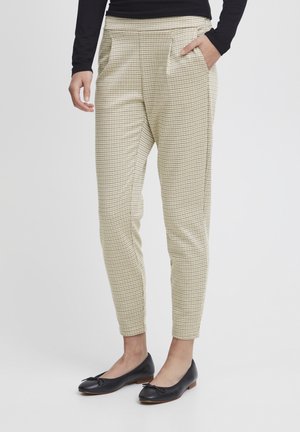 Tapered trousers in a light beige fabric with a textured check pattern, featuring side pockets and a fitted waistband. Paired with black flats.
