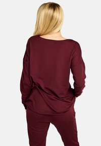 Bordo dolg rokav z ohlapnim krojem in širokim izrezom, narejen iz mehke, teksturirane tkanine z padajočimi ramenskimi šivi.