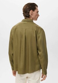 Olive green, long-sleeve shirt with a relaxed fit, featuring a back yoke, button cuffs, and smooth fabric texture.