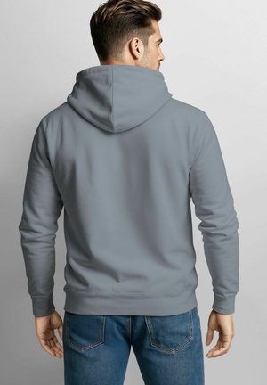 Graue Kapuzenjacke mit Kängurutasche und verstellbarem Kordelzug. Weiches Material, lange Ärmel und ribbelte Bündchen, kombiniert mit blauen Jeans.