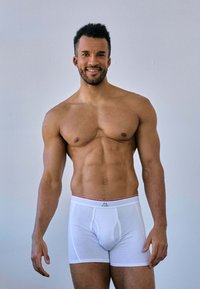 Vita boxerunderkläder med röd midjeband, åtsittande design och formad front. Slät textur och minimal sömmar synliga.