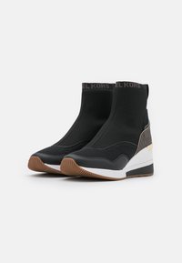 Botas deportivas negras con diseño tipo calcetín, materiales de malla y sintéticos, entresuela blanca elevada y suela de goma marrón.