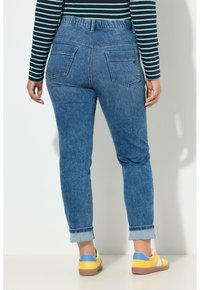 Siniset slim fit -farkut, joissa on käännetyt lahkeet, takataskut ja korkea vyötärö. Yhdistetty keltaisiin ja sinisiin kenkiin.