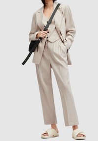 Beige tre-delad kostym med en åtsittande väst, lösa byxor och en skräddarsydd blazer. Matcher med krämfärgade slip-on sandaler och en svart väska.