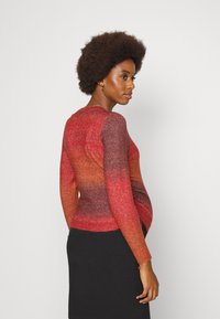 SUÉTER DE TRICÔ com um design em degradê nas tonalidades de vermelho e laranja, com mangas longas e decote redondo, combinado com uma saia preta com textura canelada.