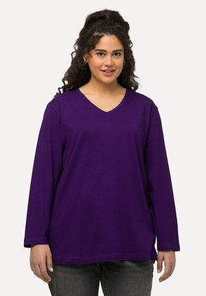 Chemise à manches longues en tissu violet uni, avec un col en V, offrant une coupe décontractée avec des fentes sur les côtés et une texture lisse et douce.