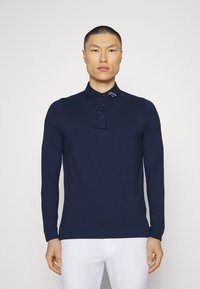 Navy long-sleeve polo shirt featuring a buttoned placket and branded collar. Smooth fabric with a fitted design and cuffs at the sleeves.