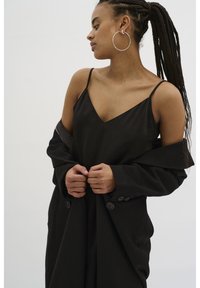 Svart spaghetti strap topp i kombination med en svart, oversized kappa. Kappan har stora knappar och ett mjukt, texturerat tyg.