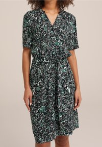 Semi-fitted jurk met korte mouwen, met een groen, zwart en wit bloemenpatroon. De jurk heeft een V-hals en een strikceintuur in de taille.