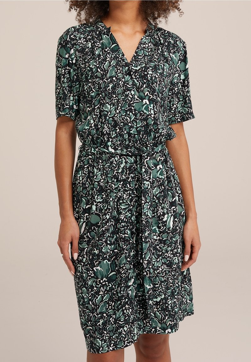 Semi-fitted jurk met korte mouwen, met een groen, zwart en wit bloemenpatroon. De jurk heeft een V-hals en een strikceintuur in de taille.