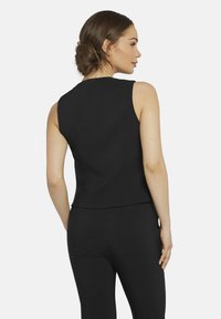 Schwarzes ärmelloses Top mit einer taillierten Passform und glatter Textur. Es hat einen dezenten Ausschnitt und einen leichten Abfall am hinteren Saum.