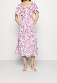 Robe midi fleurie avec un décolleté carré, des manches courtes évasées, et un mélange de couleurs rose, bleu et jaune sur un tissu léger.