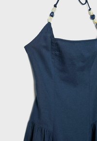 Robe sans manches bleu marine avec un corsage ajusté, une jupe évasée et des bretelles fines ornées de perles alternées blanches et bleu marine.