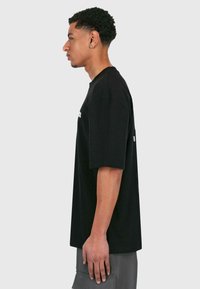 Sort bomulds T-shirt med korte ærmer, rund hals, afslappet pasform, med hvid grafisk tekst på forsiden og en ensfarvet bag.