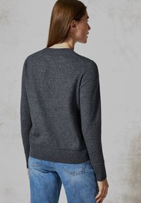 Dunkelgrauer, gestrickter Pullover mit rundem Halsausschnitt, gerippten Ärmelbündchen und Saum, kombiniert mit hellblauen Jeans. Weiches Material und klassischer Schnitt.