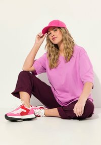 Rosa T-Shirt, lila Hose und rosa Sneakers mit roten Akzenten. Sitzende Pose, lässiges Design, weicher Stoff und lockere Passform.