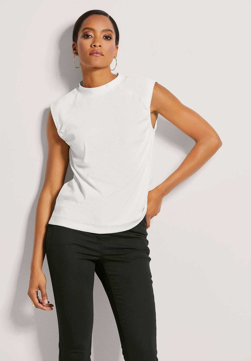 Weiße ärmellose Bluse mit Rundhalsausschnitt, aus weichem Stoff gefertigt. Kombiniert mit schwarzen, figurbetonten Hosen, die ein modernes und minimalistisches Design zeigen.