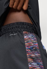 Calções desportivos pretos com cintura elástica, apresentando um painel colorido de estampado abstrato e a marca "Dri-FIT" na lateral.