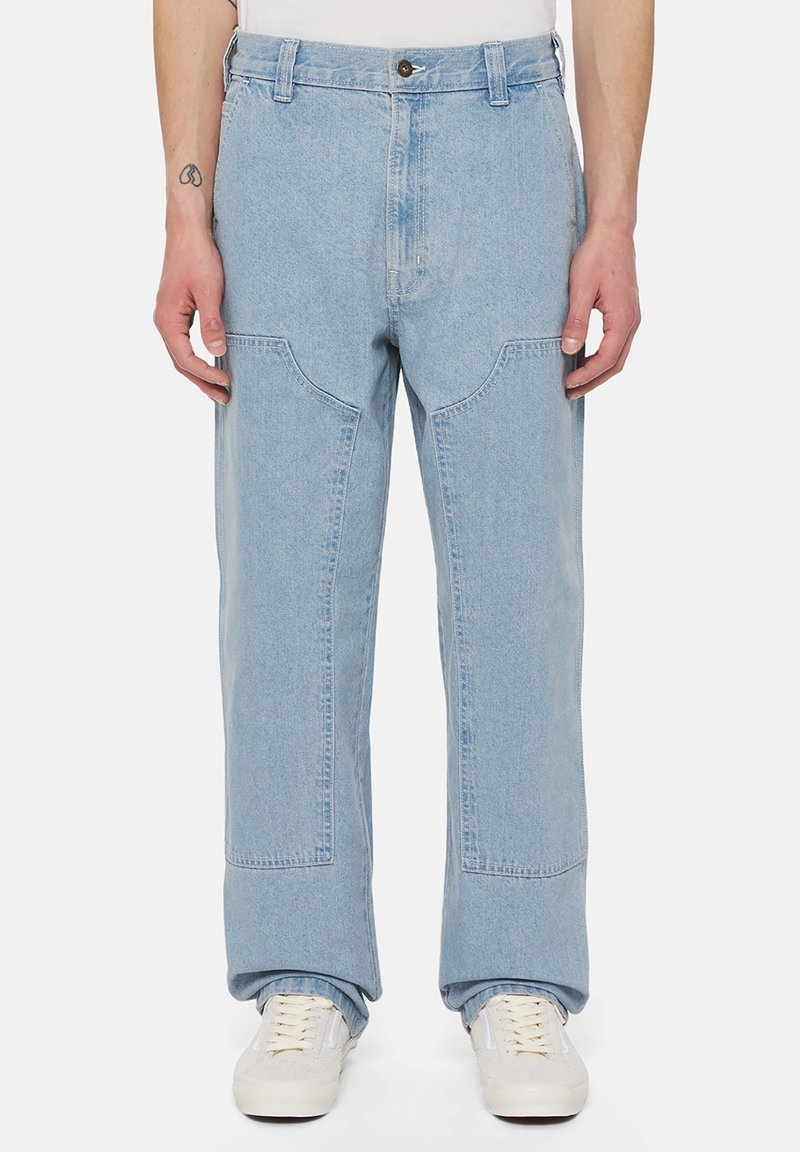 Ljusblå denimjeans med avslappnad passform, med distinkta fickor i lappar och knappstängning. Kombinerat med vita sneakers.