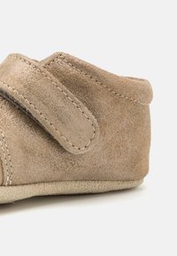 Zapato de ante beige con punta redondeada, tiras de velcro y detalle de costura en el costado. Textura suave con una suela flexible.