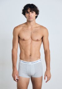 Boxer-briefs en coton gris avec une ceinture élastique blanche portant le nom de la marque "GANT" imprimé en bleu, portés par un modèle.