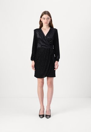 Black wrap dress with long sleeves, textured fabric featuring a subtle pattern, and a tie at the waist. Paired with black pointed heels.
