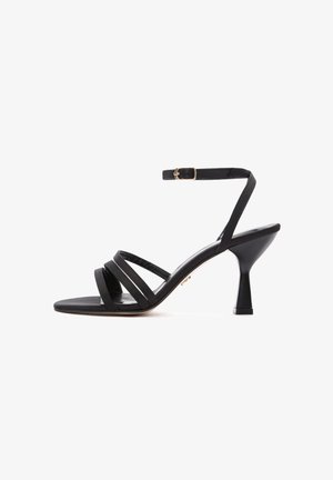 Black heeled sandals with an open toe, three straps across the front, and an adjustable ankle strap. Features a tapered block heel.