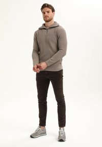 Lichtgrijze gebreide trui met een halflange rits kraag, gecombineerd met donkerbruine corduroy broek en grijze sportschoenen. Glad textuur en aangesloten ontwerp.