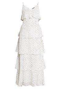 Vestido blanco sin mangas con lunares negros, que presenta un diseño de volantes en capas. La tela es ligera y fluida.