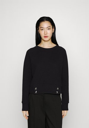 Maglione nero con texture, dal design cropped, caratterizzato da maniche lunghe e accessori in argento ai lati. Look semplice e monocromatico.