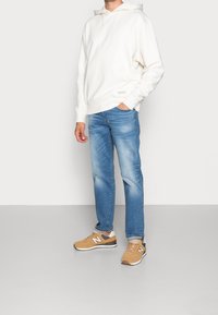 Vit huva sweatshirt, blå jeans och bruna New Balance sneakers. Sweatshirten har en framlappa och en mjuk textur.