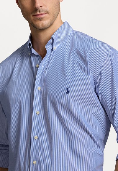 Chemise à rayures bleues avec boutons, en coton, présentant un petit logo sur la poitrine, un col standard et des manches longues.