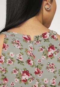 Robe fleurie avec un fond gris, arborant des roses rouges et roses ainsi que des feuilles vertes. Comprend une fermeture éclair au dos et des bretelles fines.