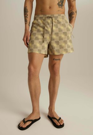 Beżowe szorty kąpielowe w kratę z elastycznym pasem i sznurkiem do regulacji, bocznymi kieszeniami oraz teksturowanym wzorem z żółtymi akcentami.